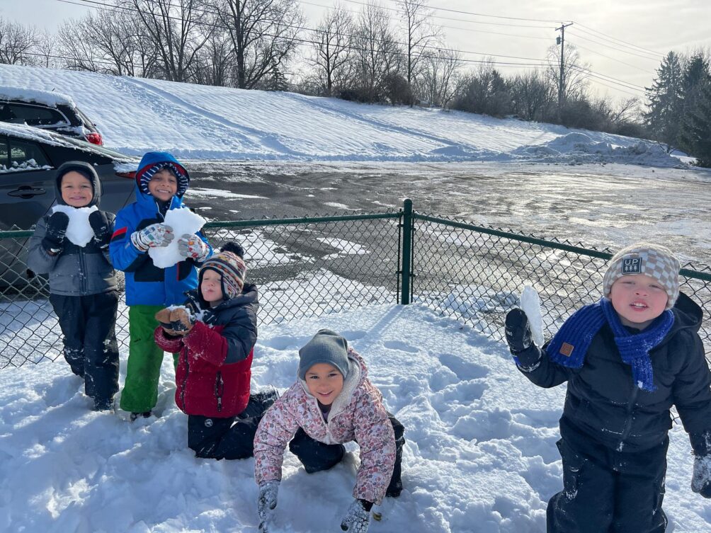 Children are playing in the snow during outdoor play time at a Montessori school