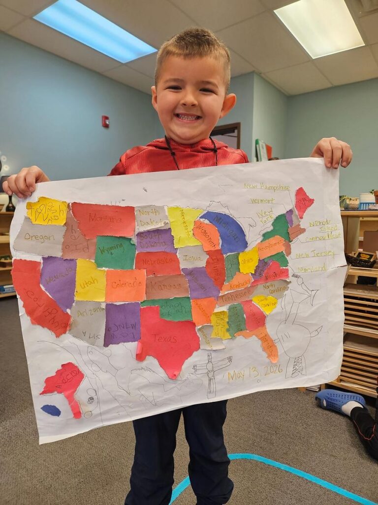 a 5 year old child holds up a completed map of the United States that he made himself in a Montessori classroom