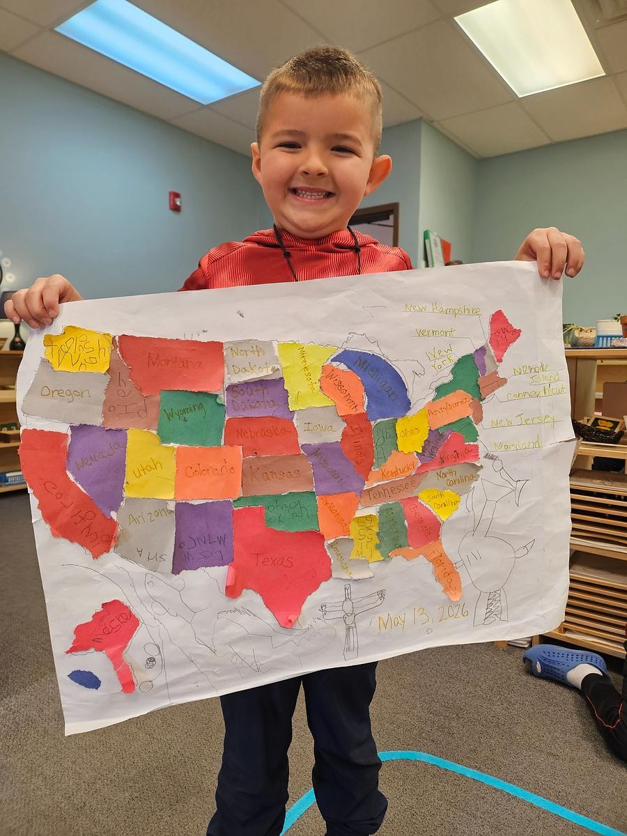 a 5 year old child holds up a completed map of the United States that he made himself in a Montessori classroom