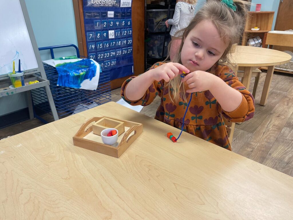 child stringing beads as a practical life activity in a Montessori classroom
