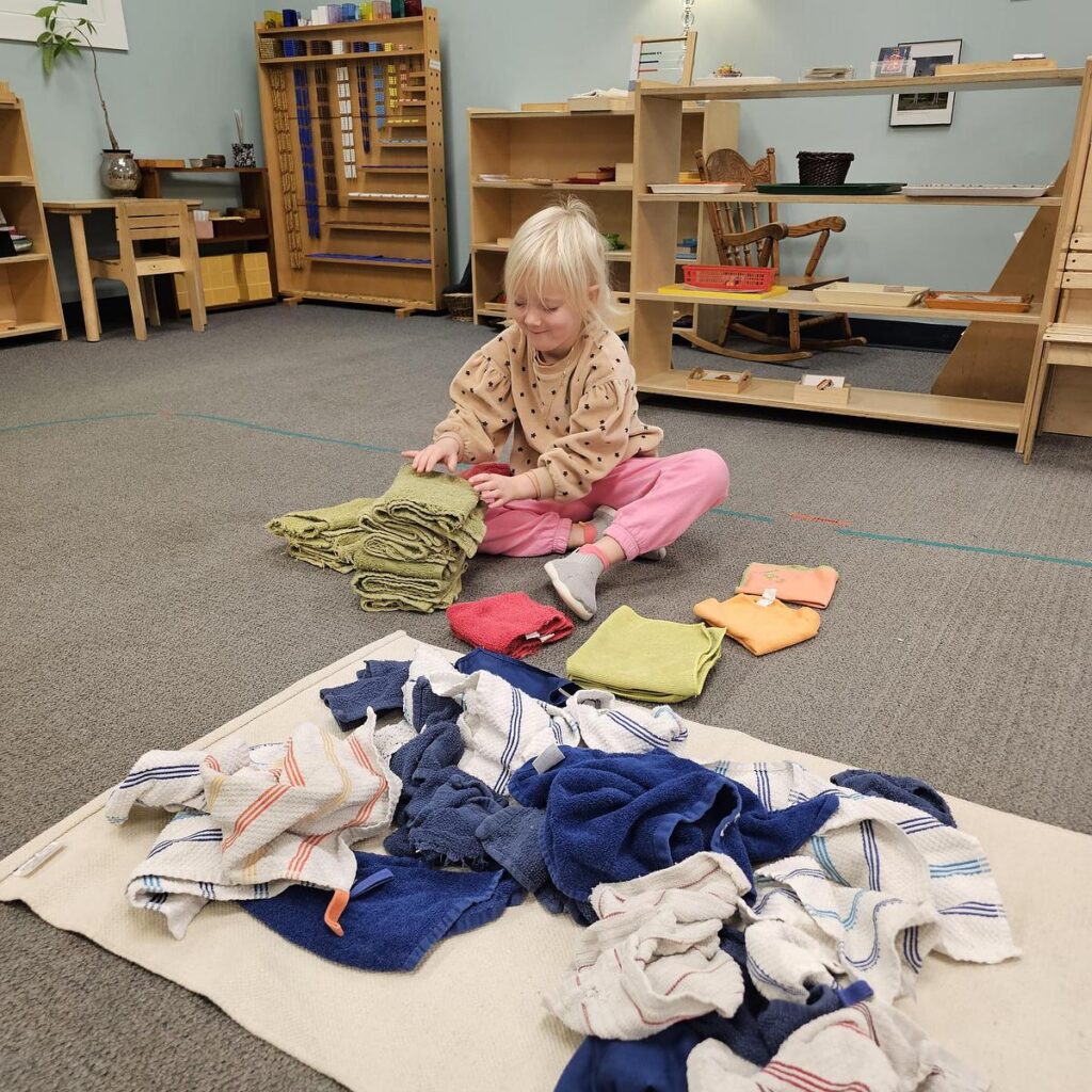 student folding towels on the floor in a Montessori primary classroom